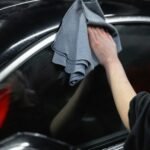 Hand cleaning black car exterior with cloth, showcasing car care and detailing.